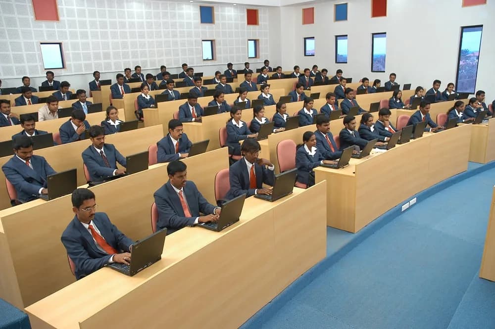 Students in formal clothes sitting in a tiered classroom with laptops
