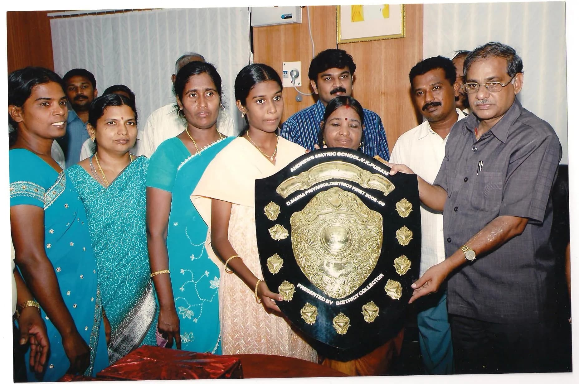 Students and a teacher holding up a school trophy shield