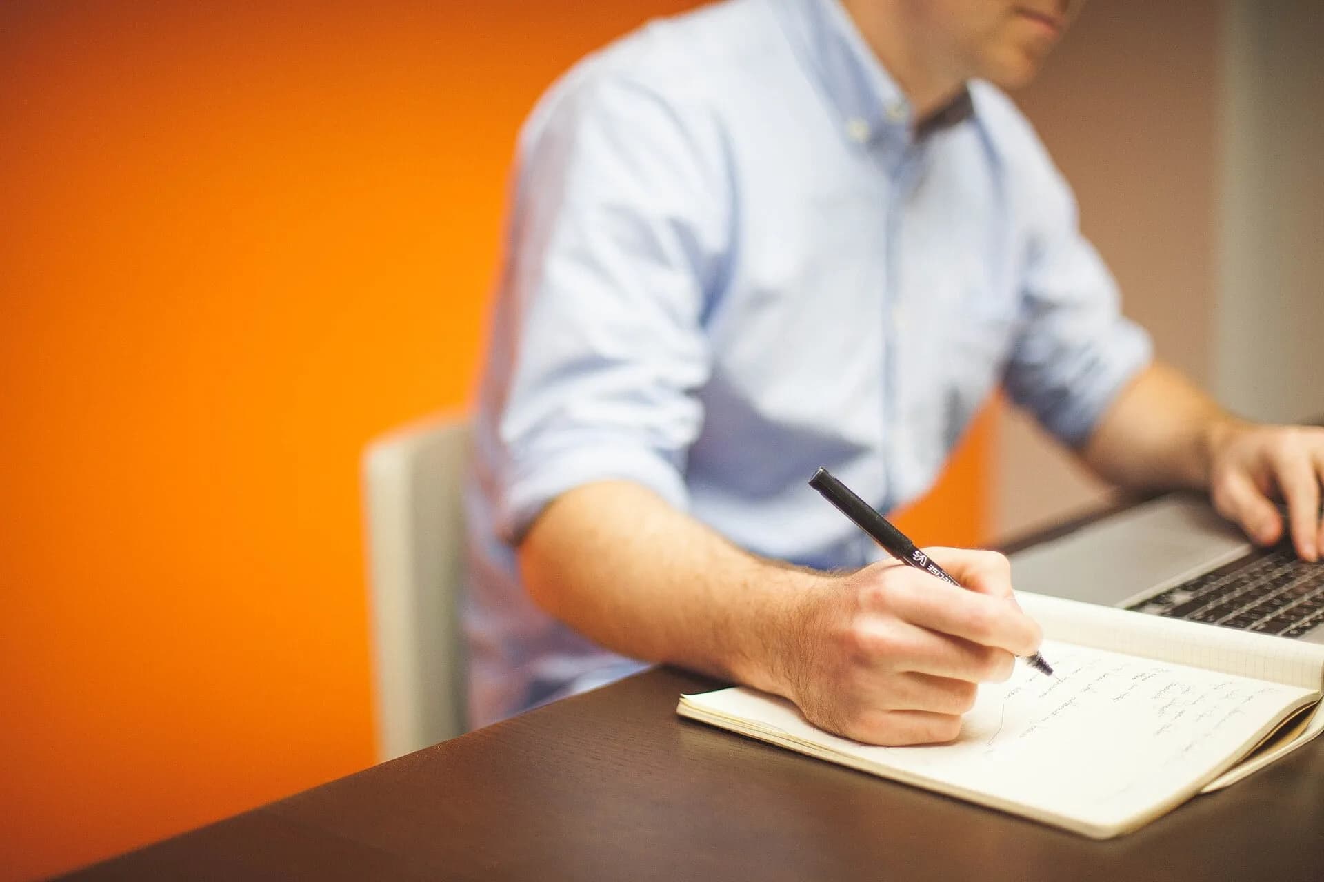 A man taking notes while using a laptop