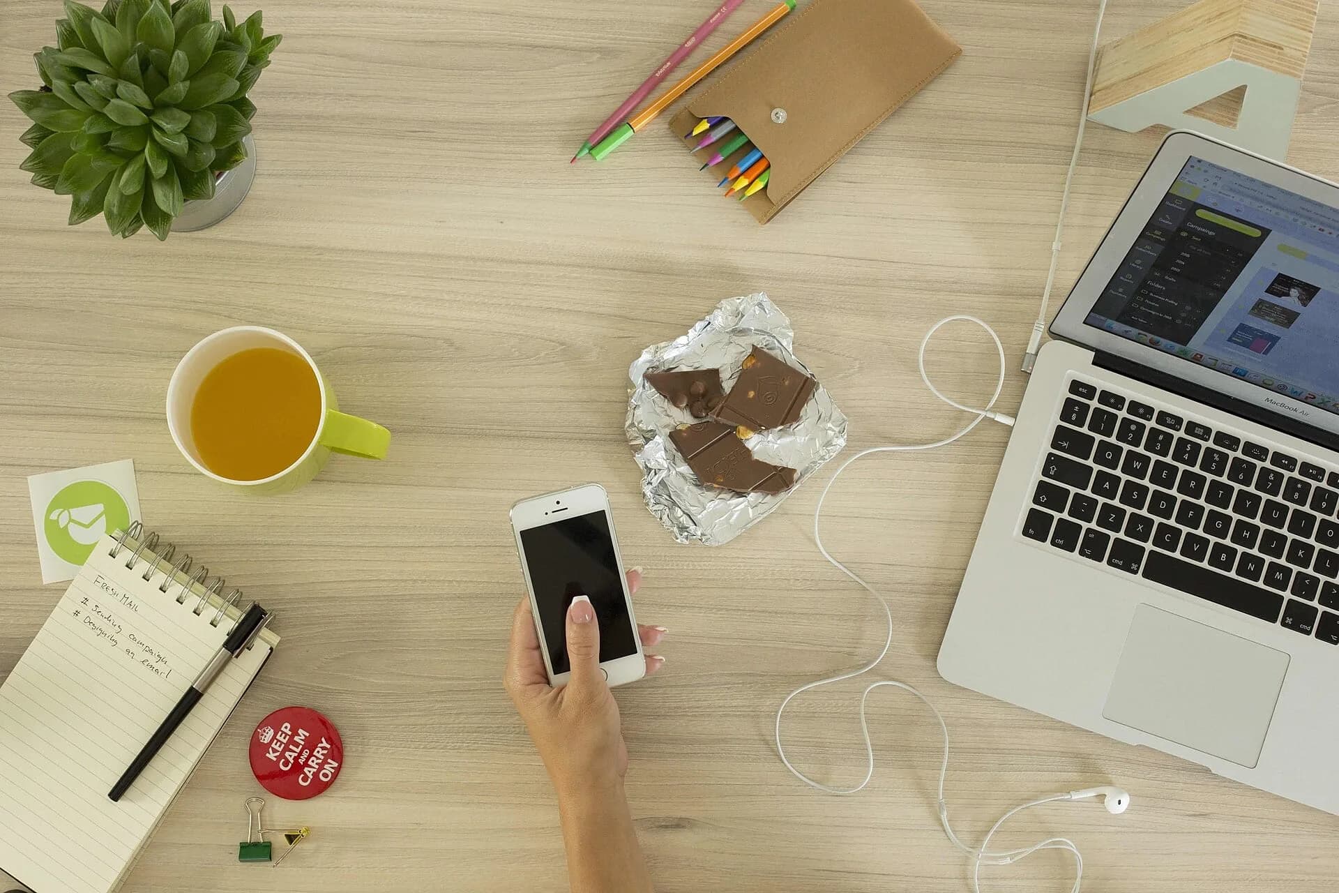 A woman holding a mobile phone at a desk with a laptop