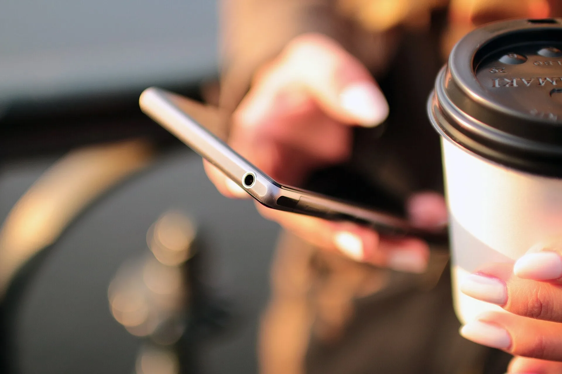 A person holding a smartphone next to a cup of coffee