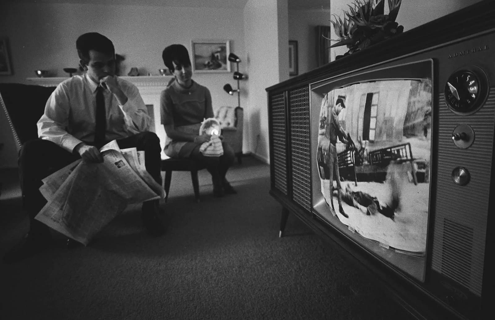 Black-and-white photo of two people watching a large television set in a living room