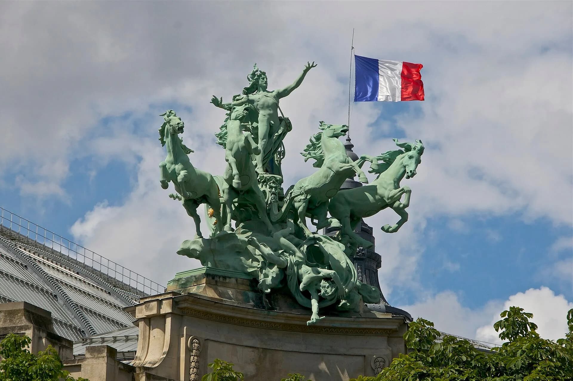 Bronze quadriga statue on the roof of the Grand Palais in Paris against a blue sky, with a French flag