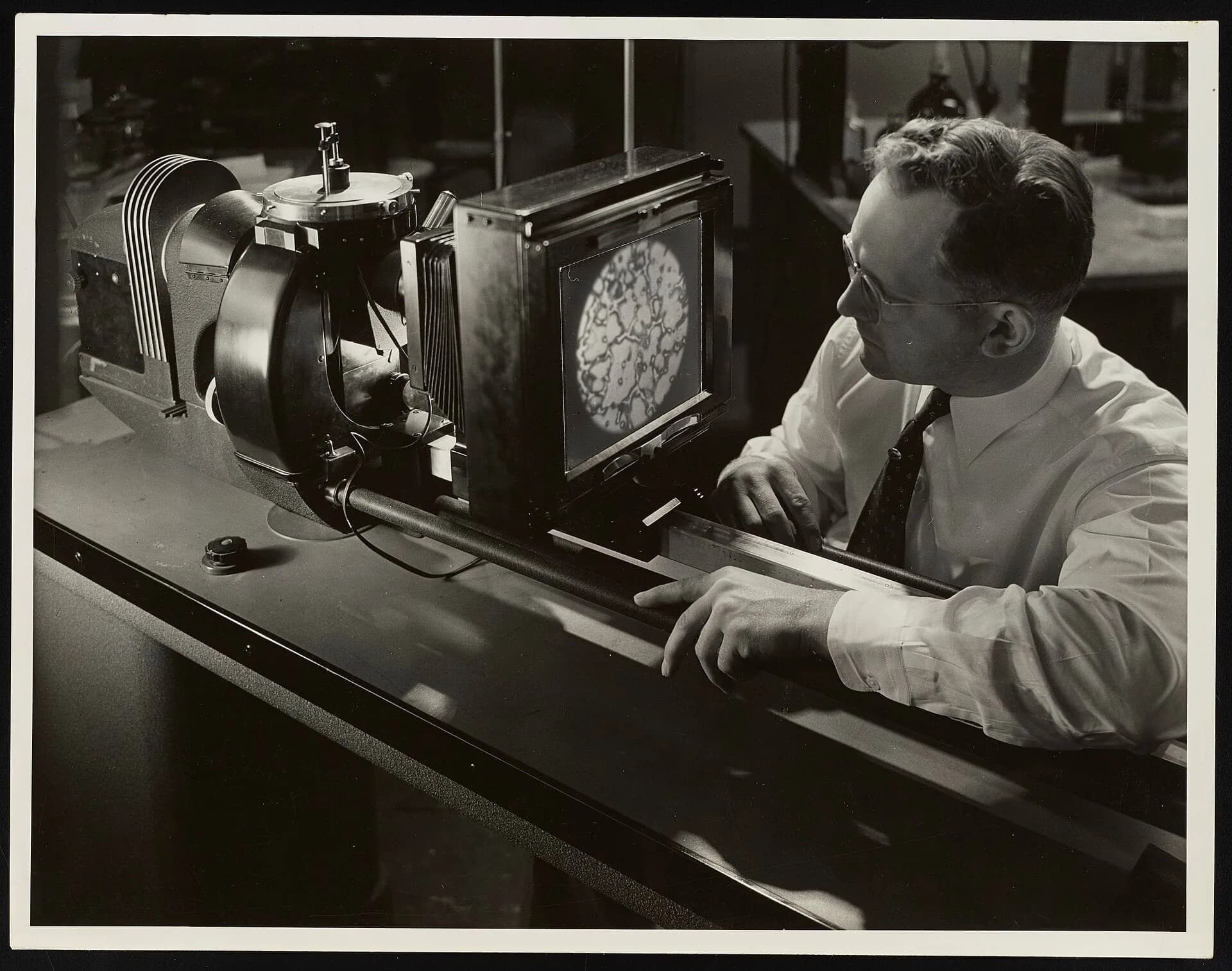 A scientist working at a large laboratory microscope, in an old photograph