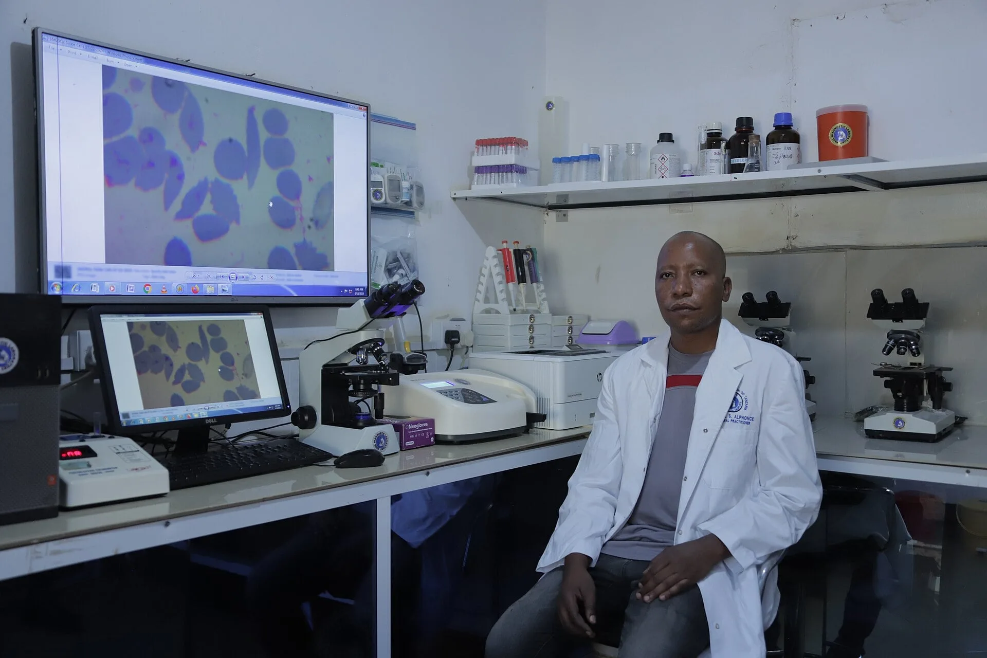 A laboratory technician at a microscope with screens