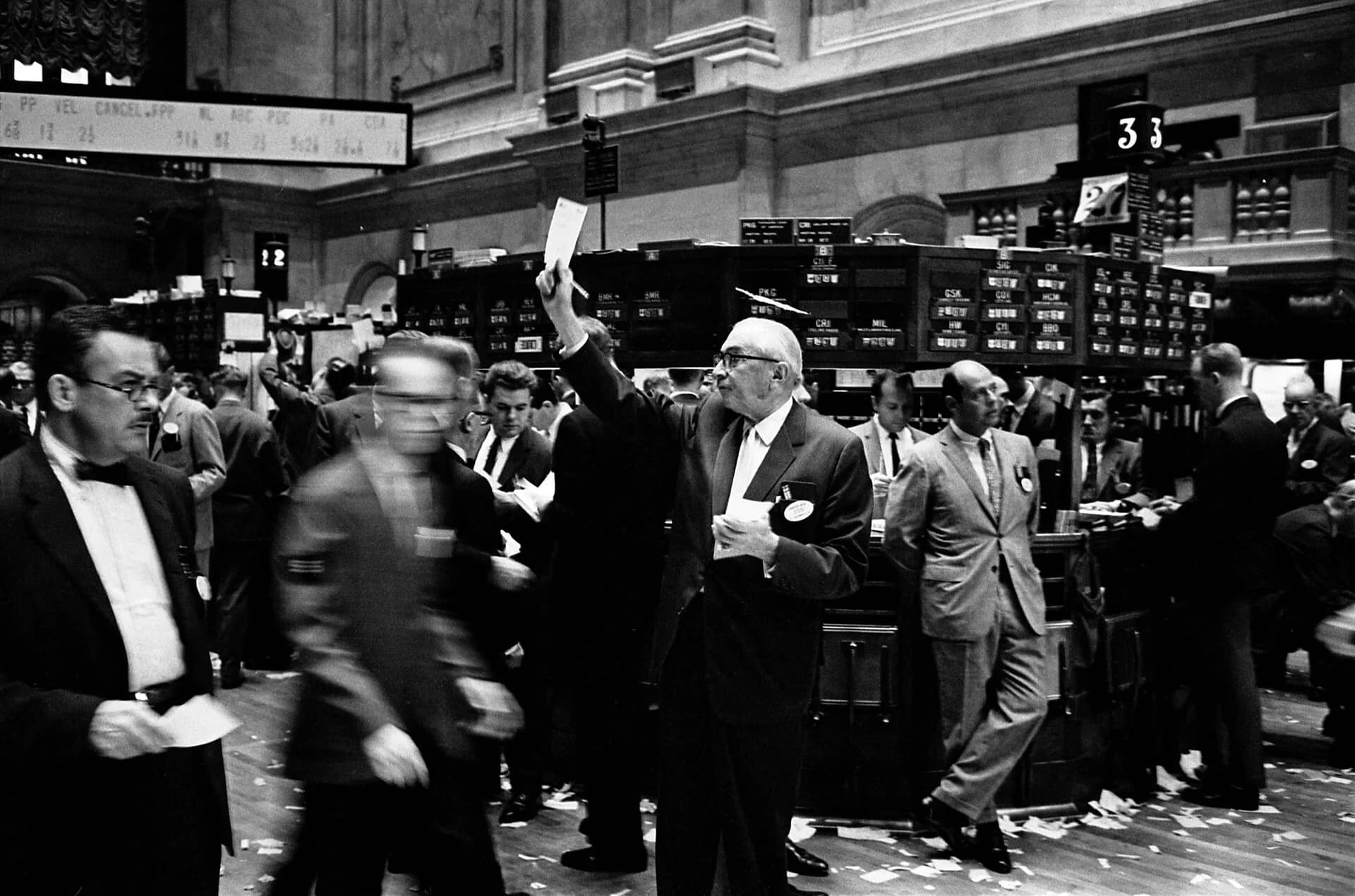 A black-and-white photo of traders on a crowded stock exchange floor in the 1960s