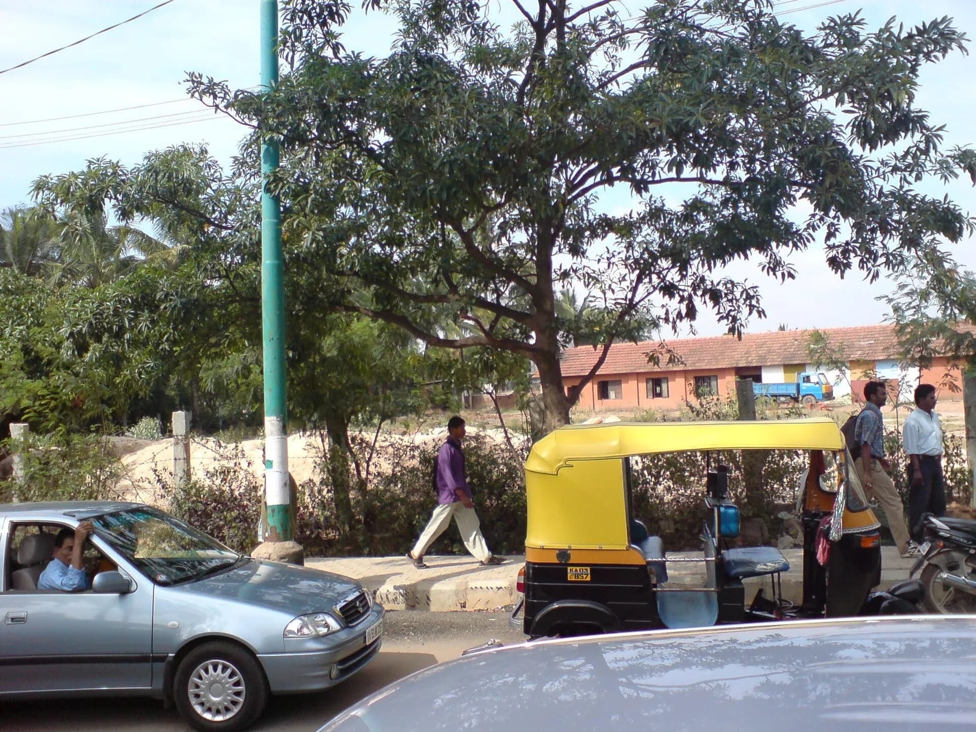 Cars and an auto-rickshaw on a tree-lined road in Bengaluru