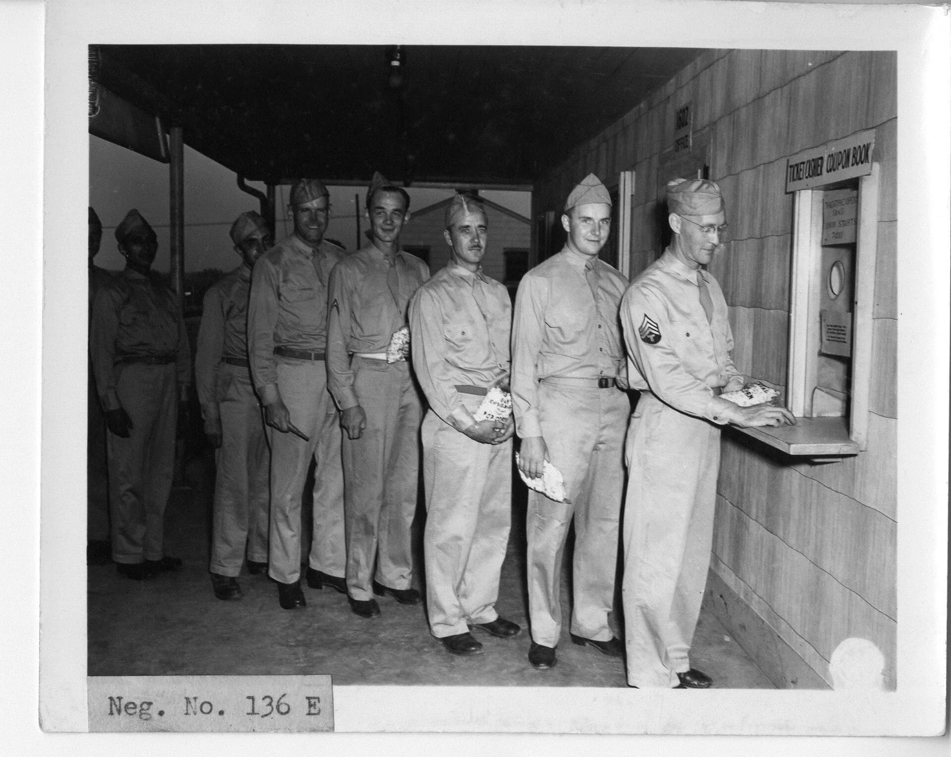 Black-and-white photo of men in uniform queuing at a cinema ticket window