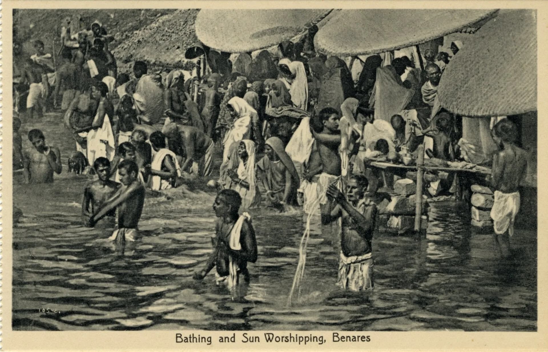 An old postcard of people bathing and worshipping the sun at a river in Benares