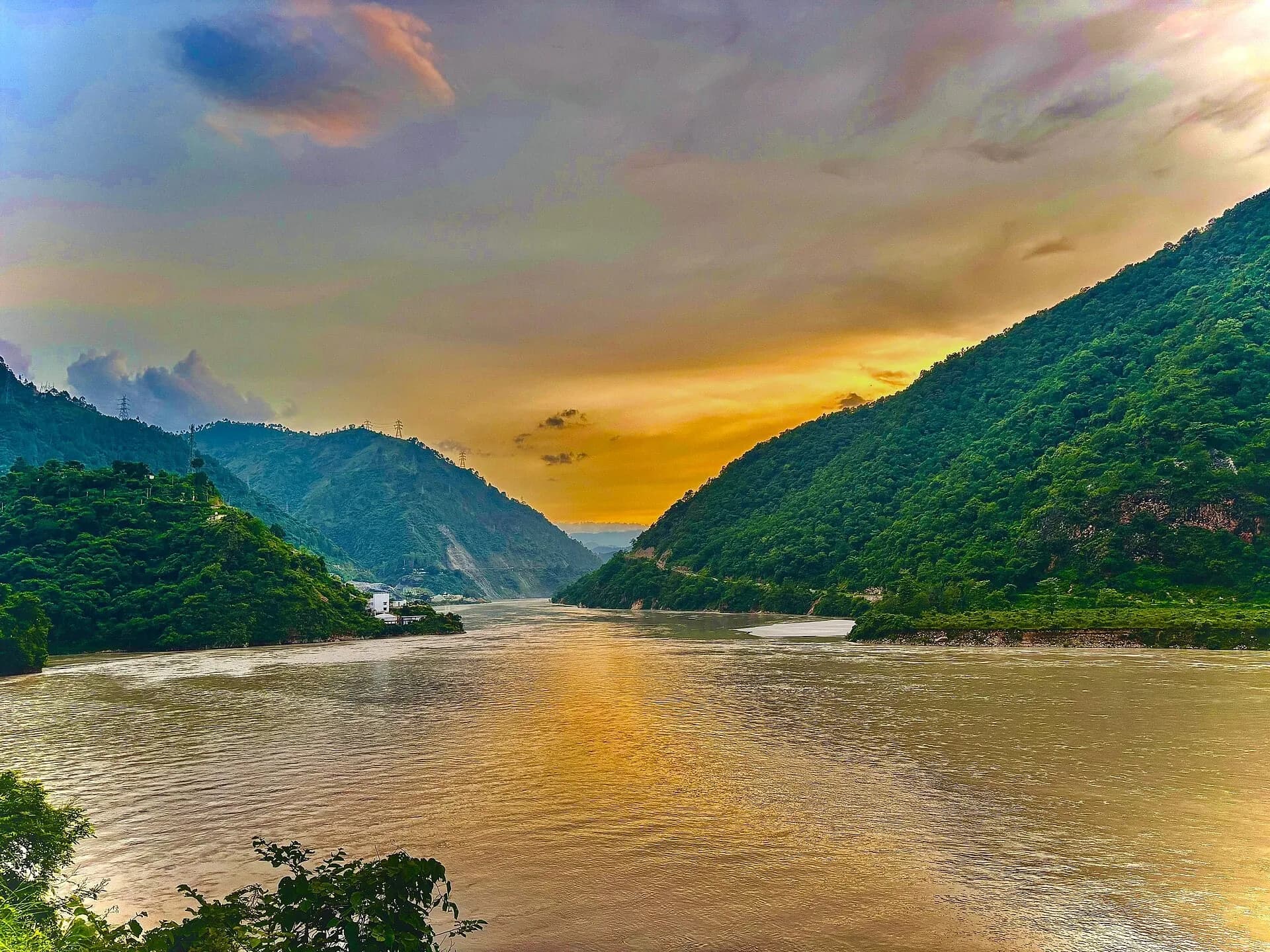 The sun setting over a river between green hills