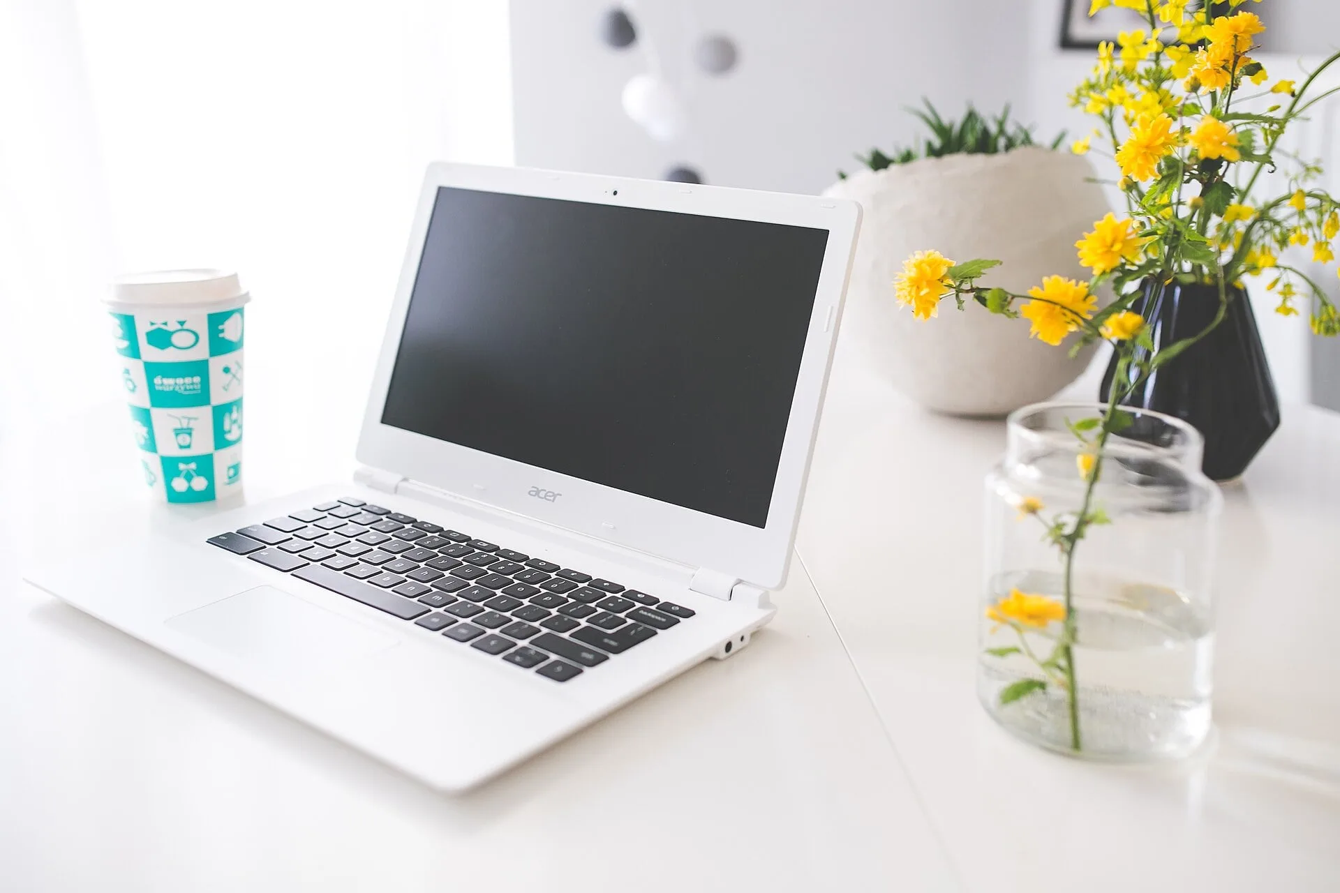 A laptop, a cup and a vase of flowers on a desk