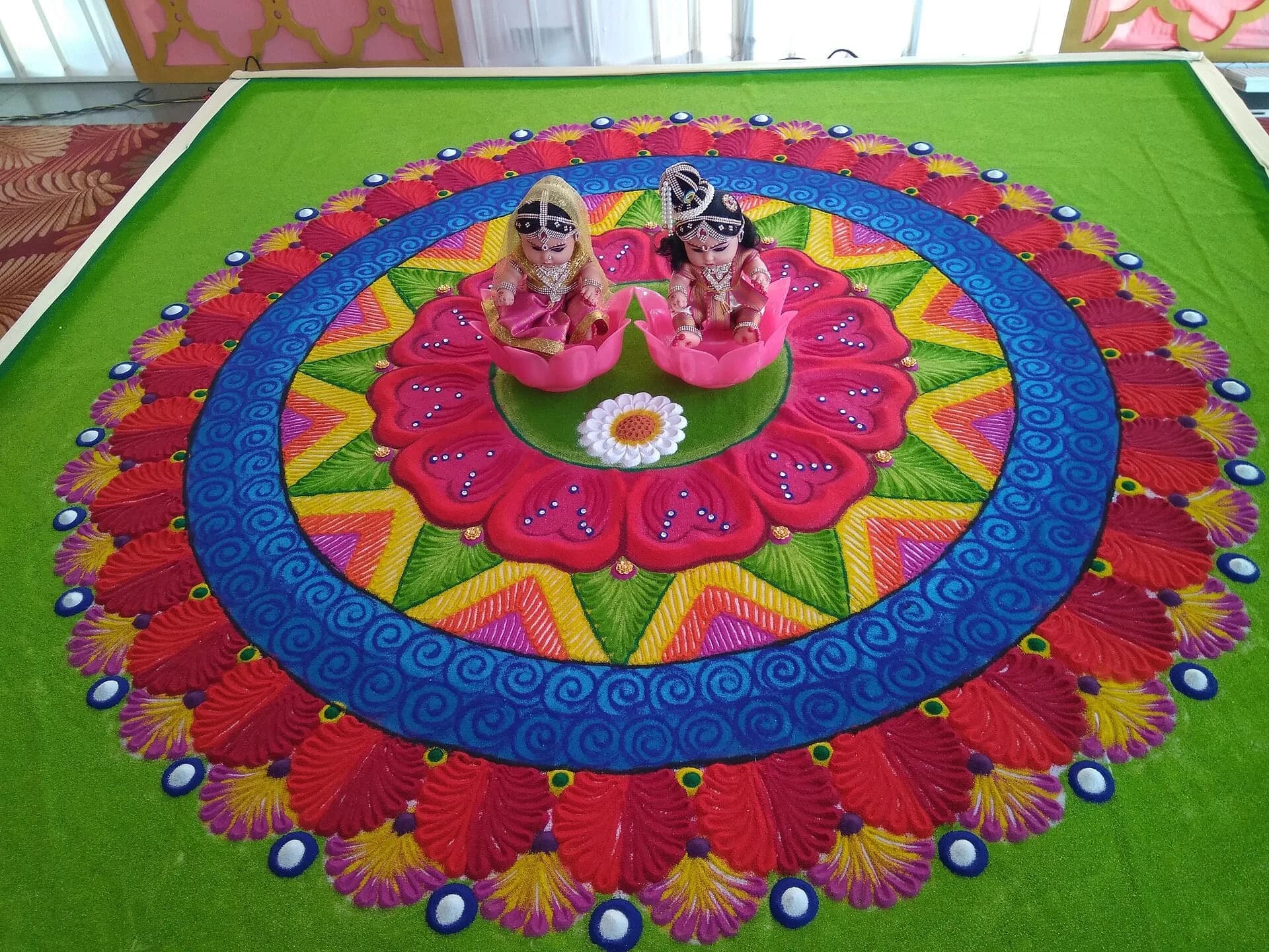 A large colourful rangoli with decorated figures at its centre