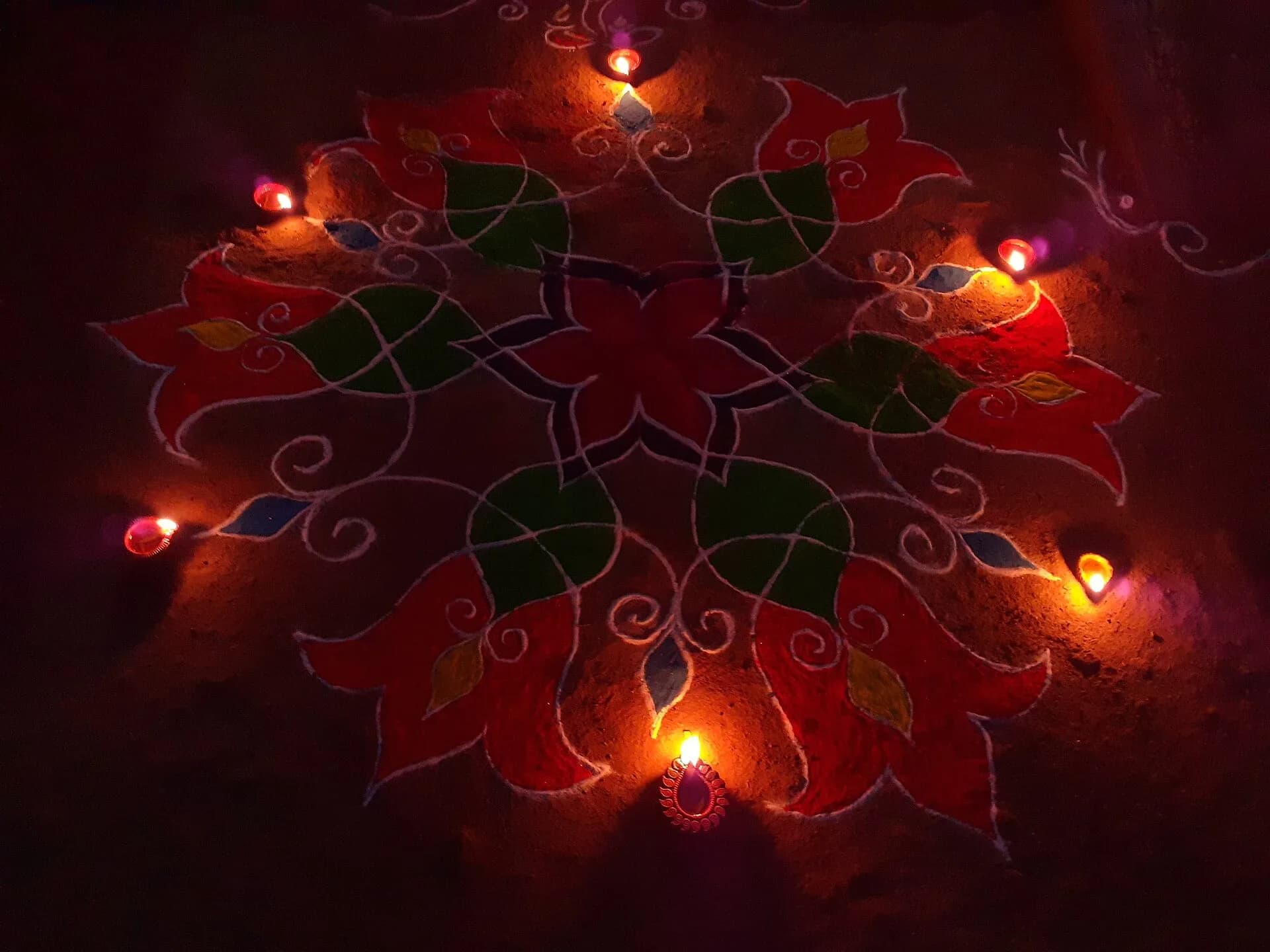 A colourful rangoli decorated with lit diyas on the floor at night during Diwali