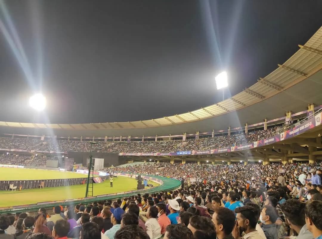 A cricket stadium full of fans under floodlights