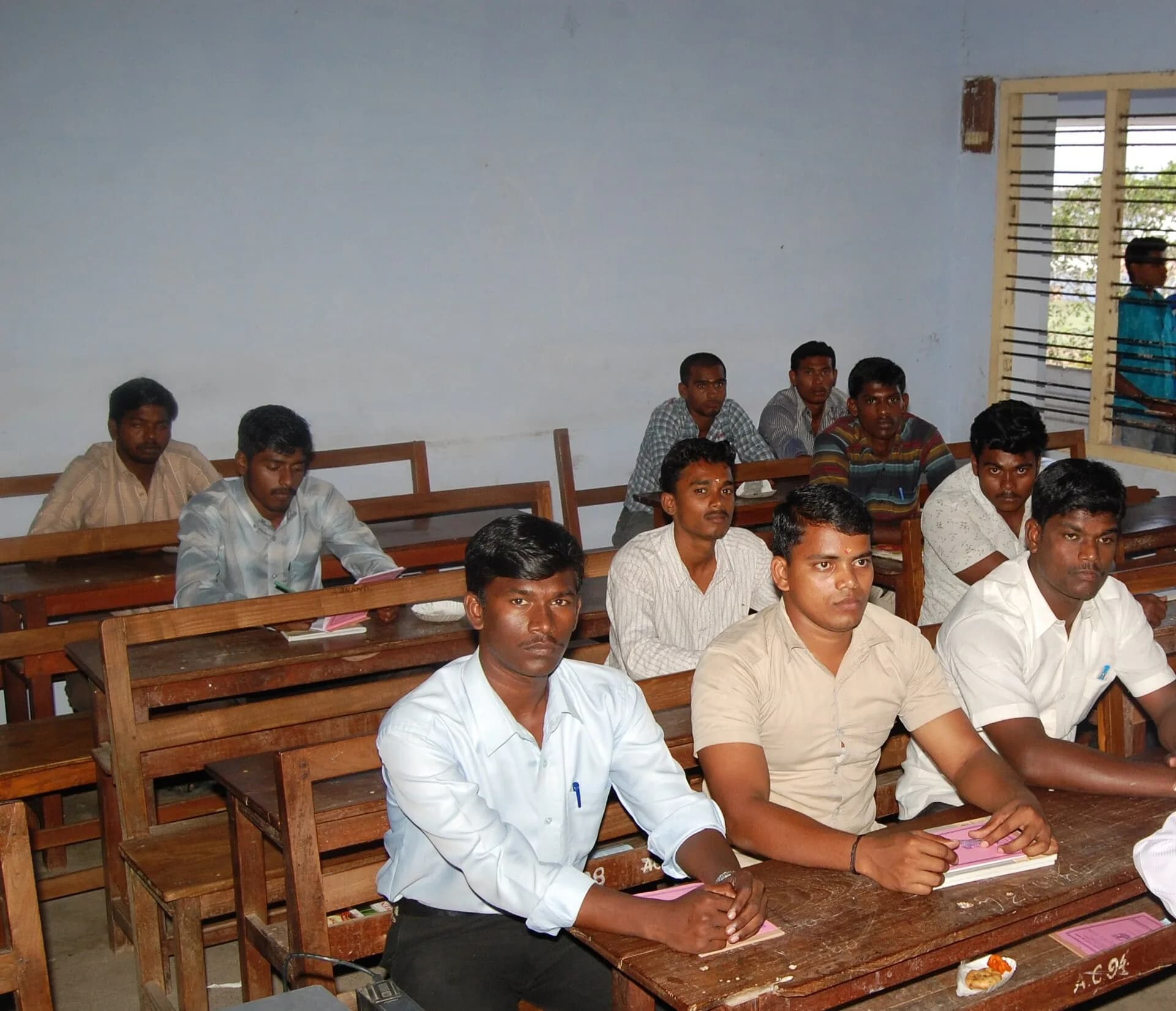 Students sitting at wooden benches in an Indian college classroom