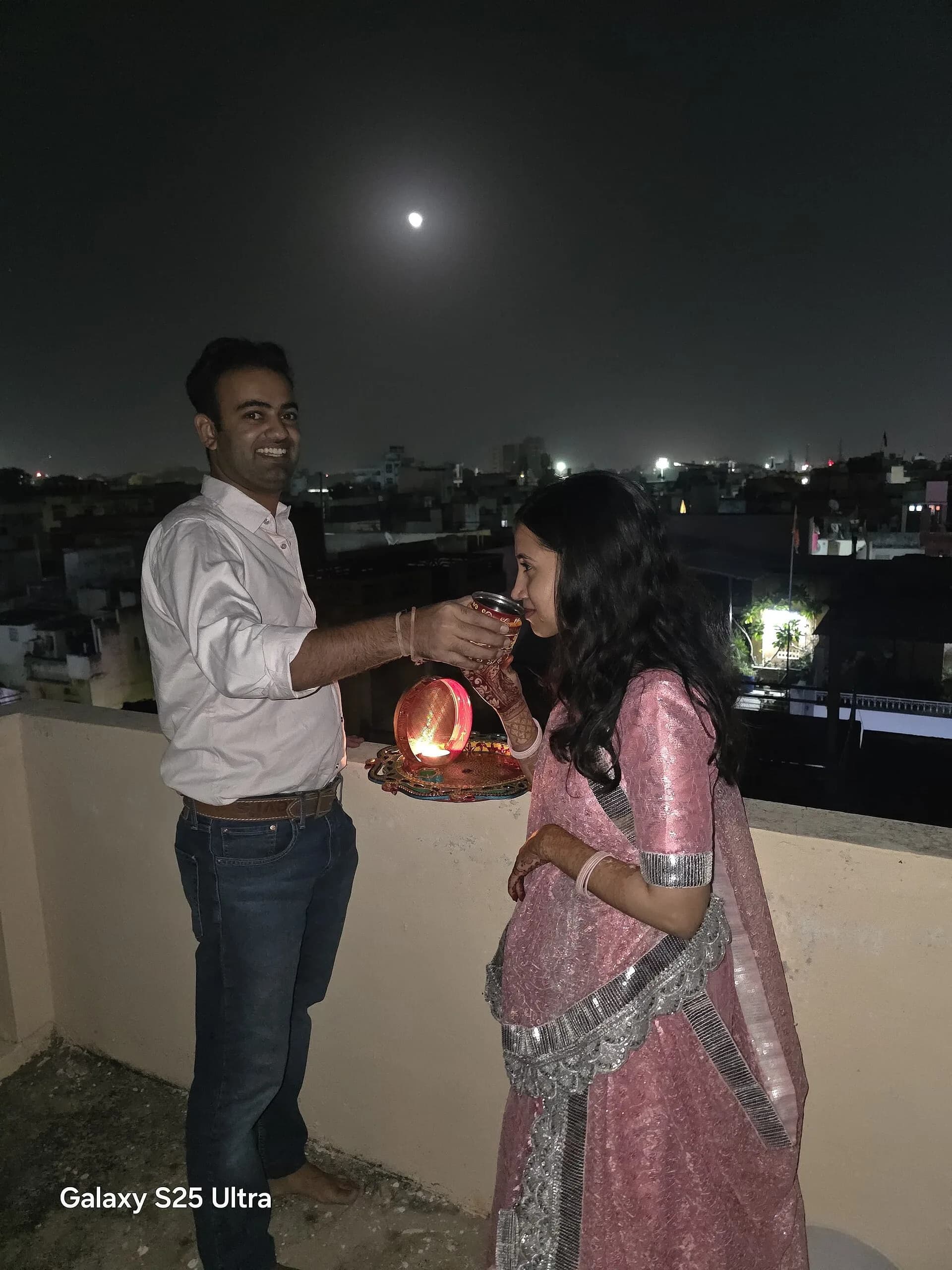A couple on a rooftop at night with a sieve and the moon behind them