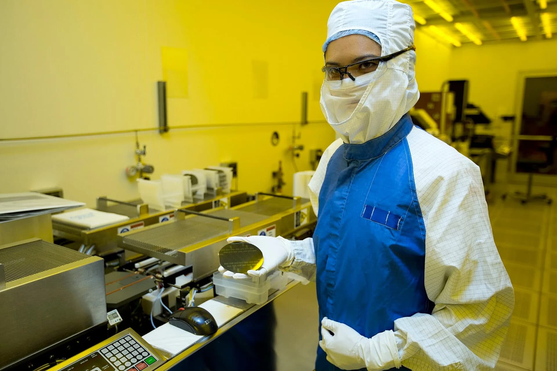 A researcher in a clean-room suit holding a silicon wafer