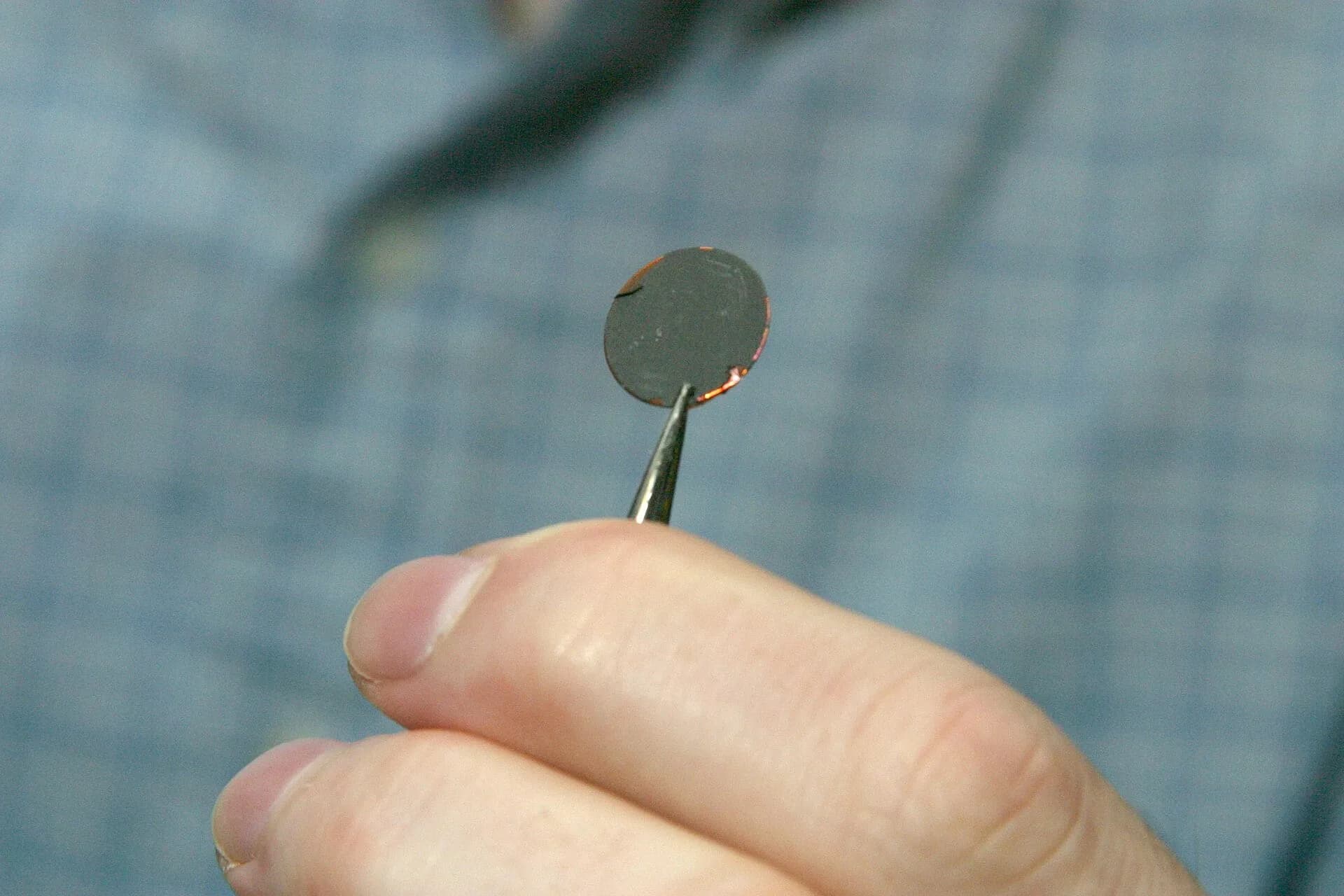 A researcher holding a small coin-cell battery between their fingers