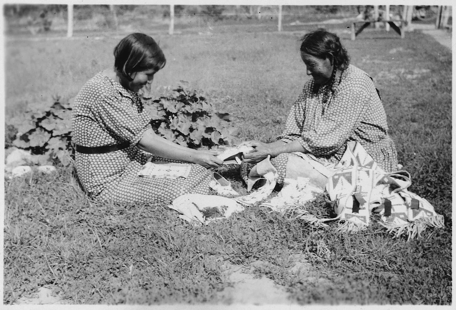 An elderly woman teaching her granddaughter beadwork