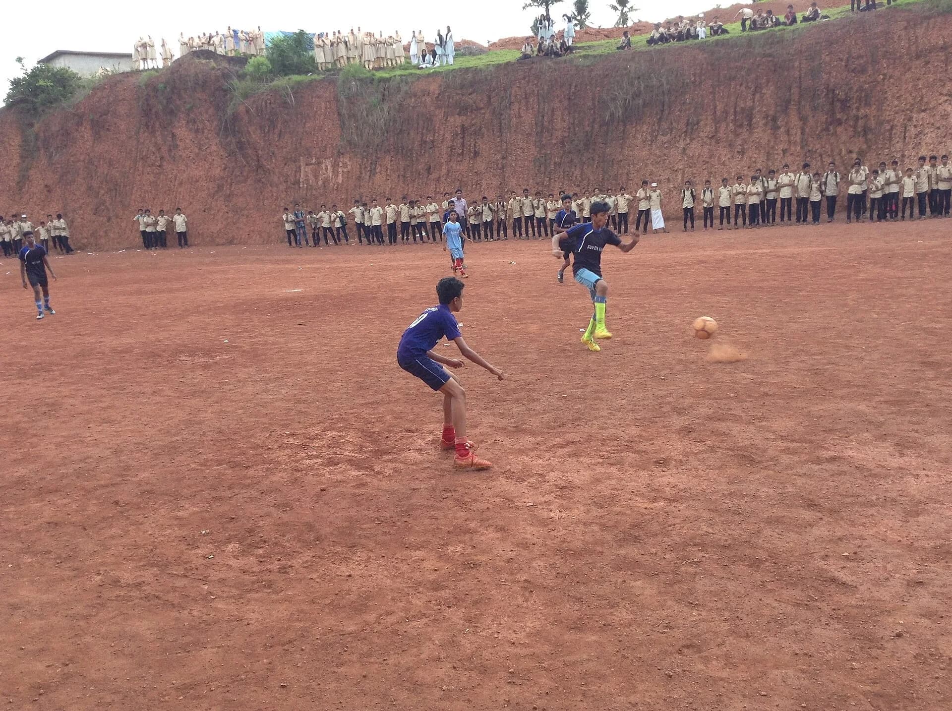 Children playing football on a red dirt field