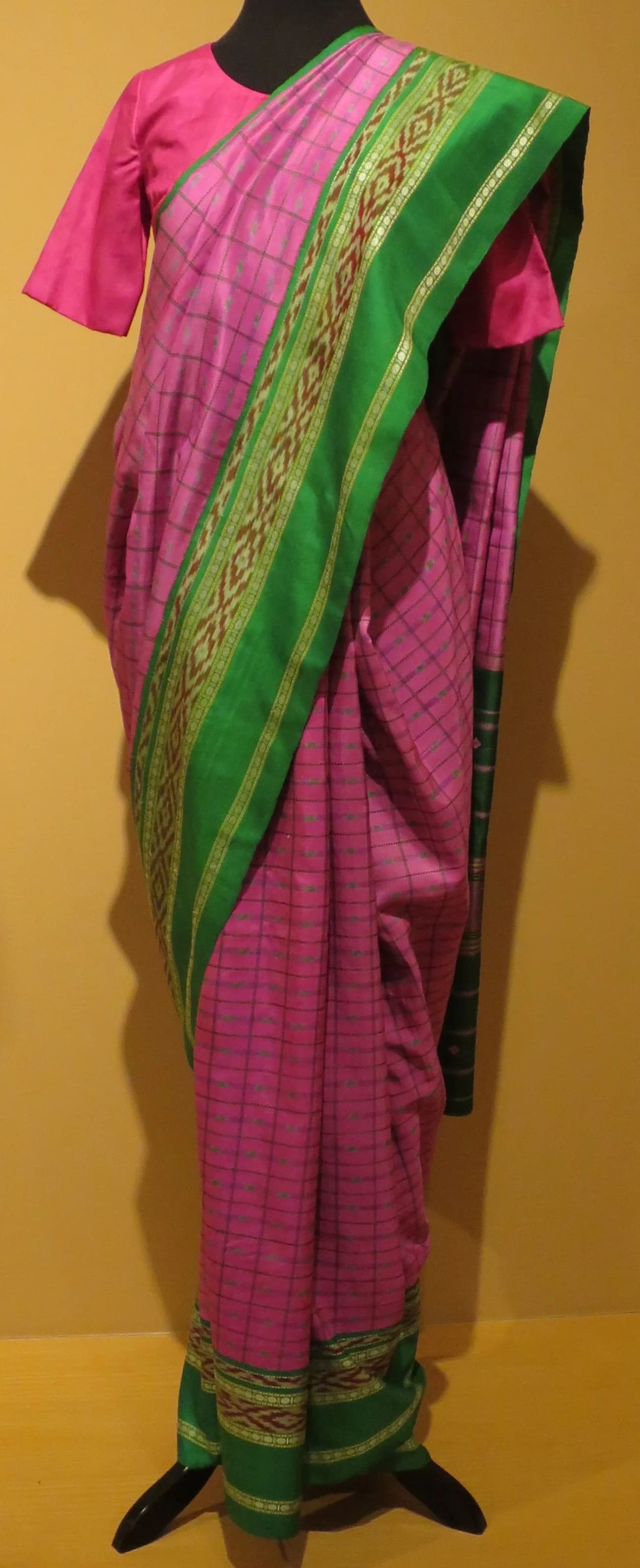 A pink and green Kanchipuram silk sari displayed on a mannequin in a museum