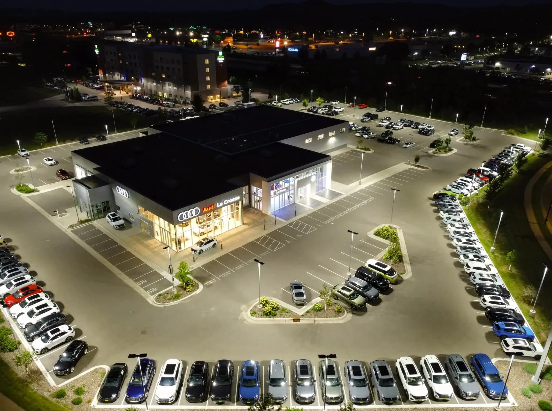 A car dealership building lit up at night with cars parked around it