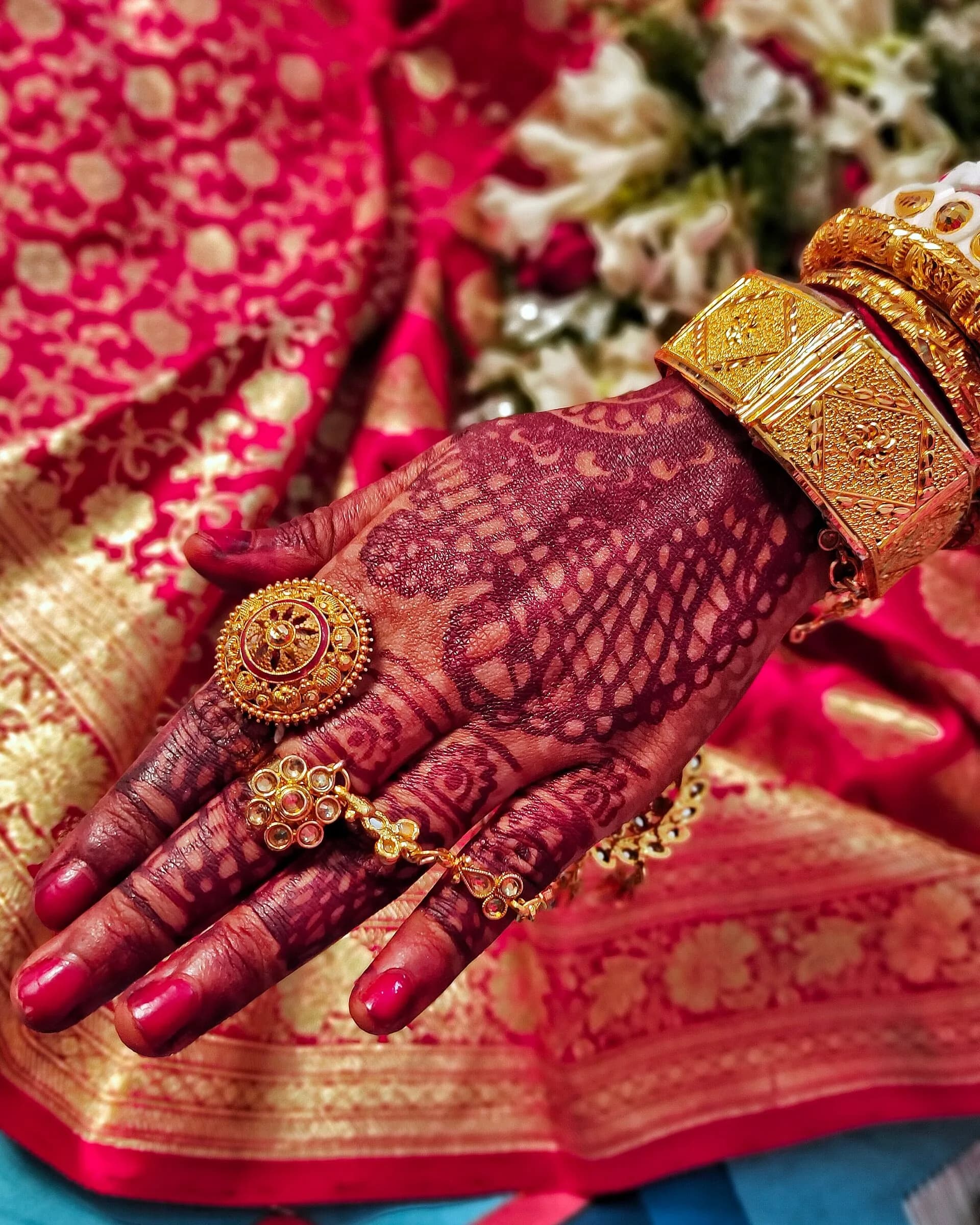 A bride's hand covered in detailed mehndi, with gold bangles and a red silk sari