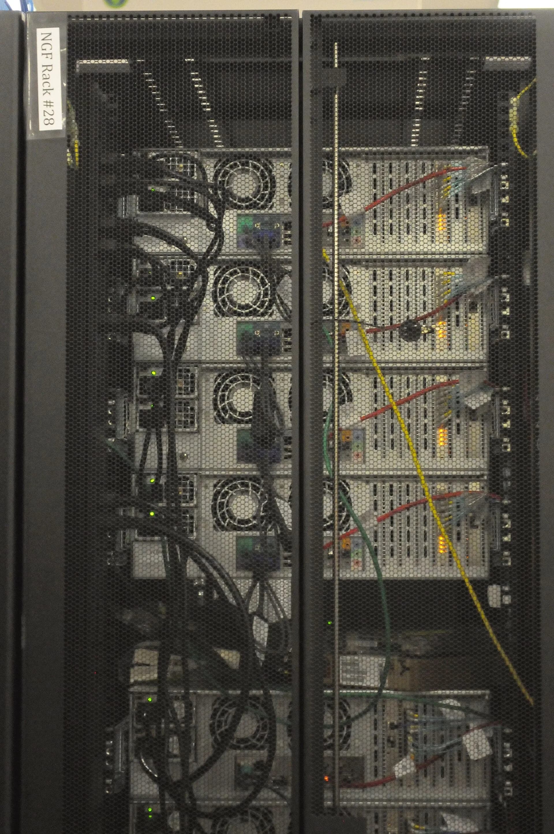 The back of a rack of computer servers with many cables